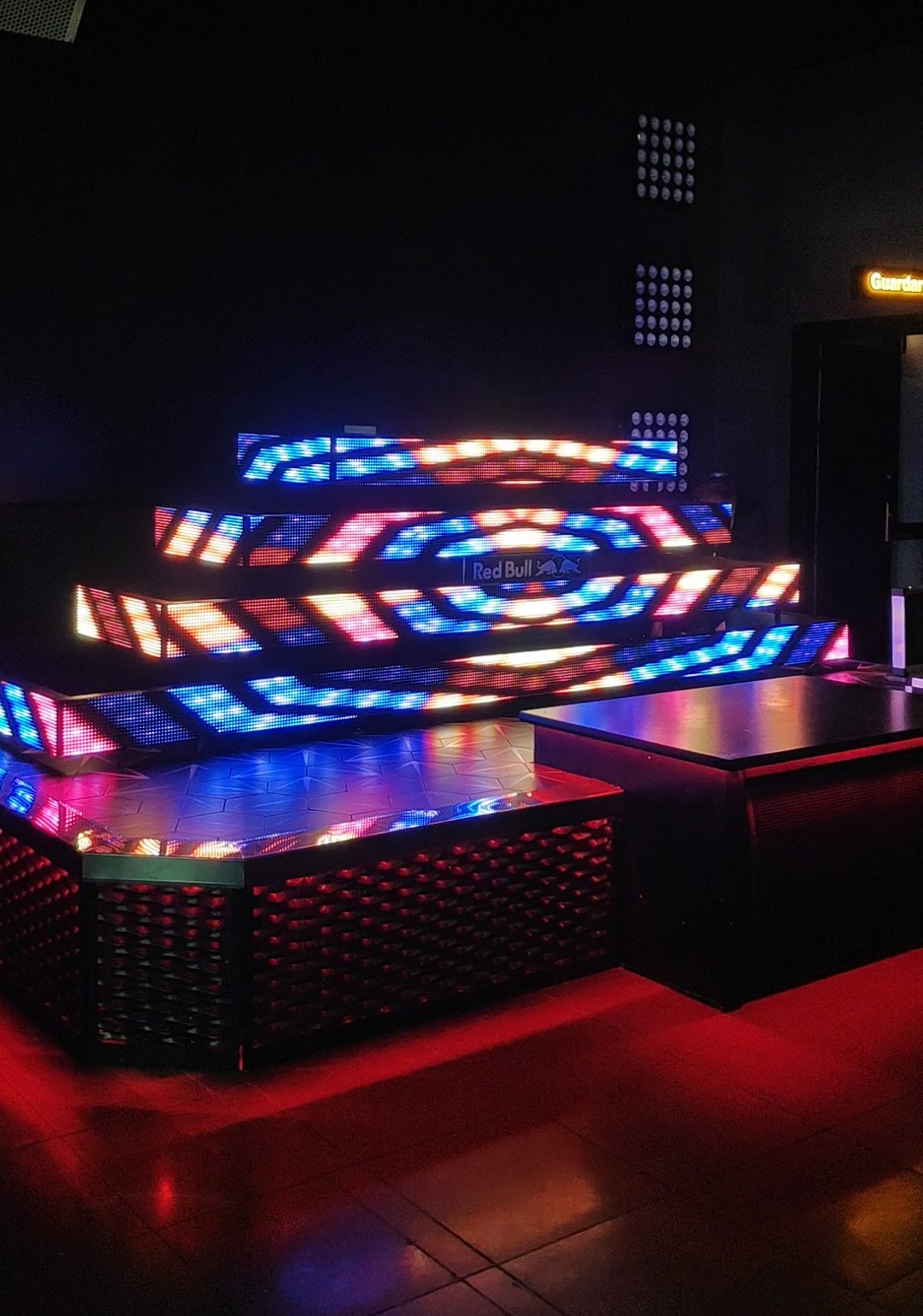Mesa de DJ formada por varias tiras de pantalla led. Tiene forma de pirámide y se reproduce un vídeo con mucho colorido.